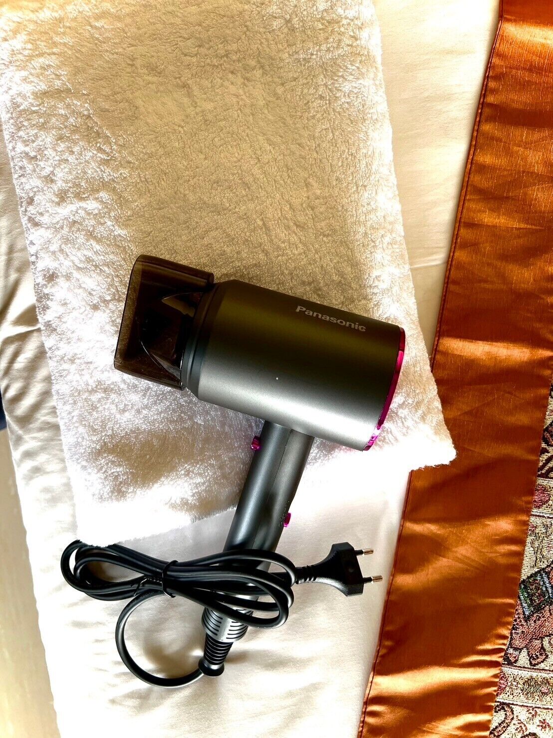 Un secador de pelo Panasonic con cable sobre una toalla blanca.