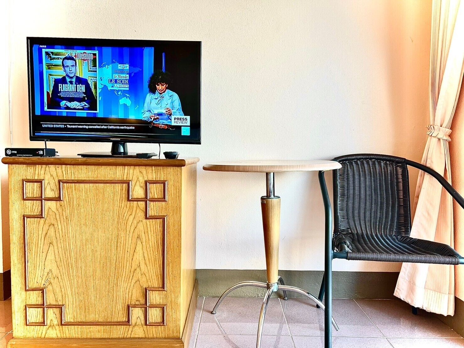Huoneessa on puinen tv-taso, pieni pyöreä pöytä ja musta rottinkituoli.
