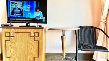 Huoneessa on puinen tv-taso, pieni pyöreä pöytä ja musta rottinkituoli.