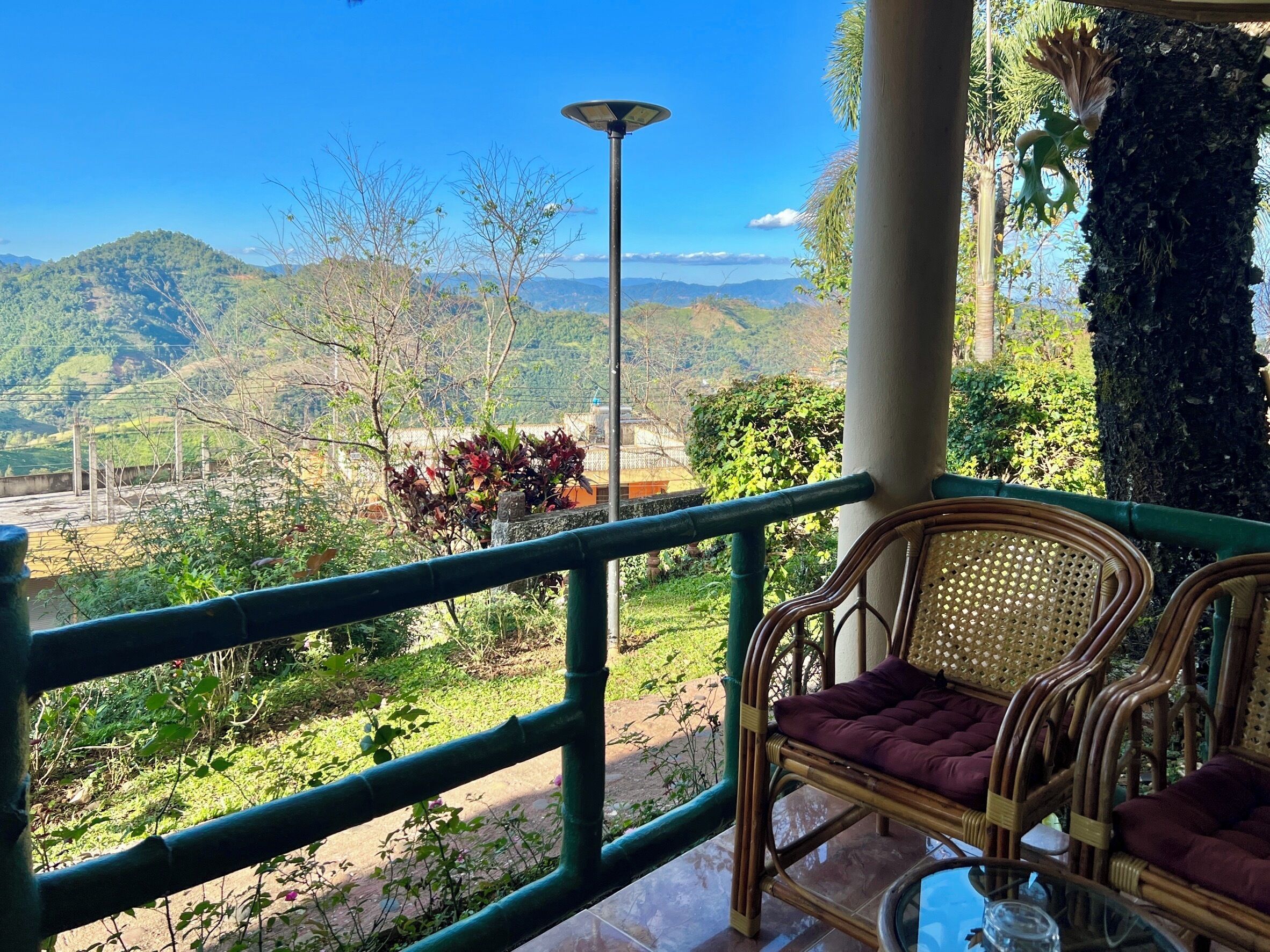 A balcony with wicker furniture, a potted plant, and a view of a hilly landscape.