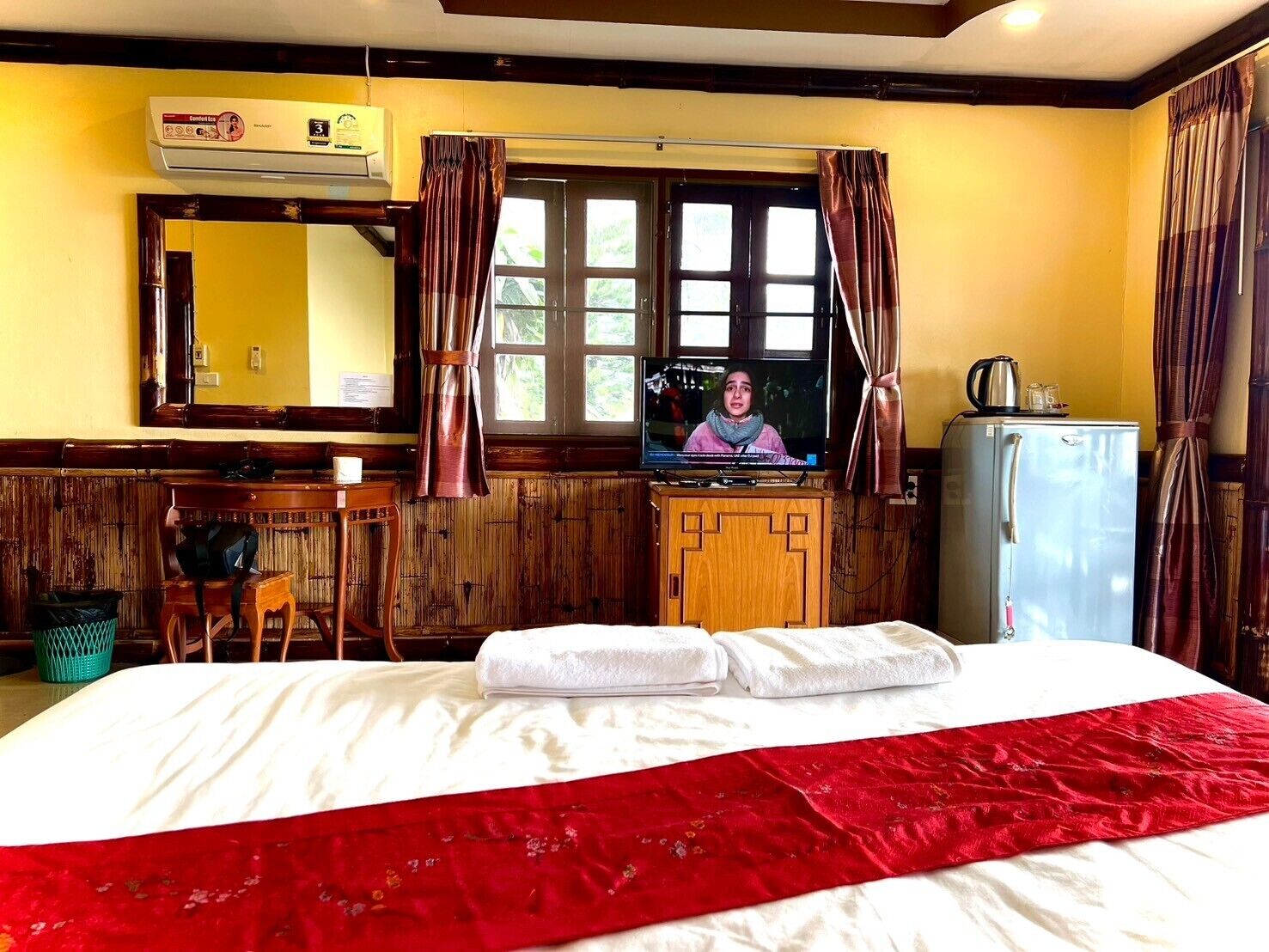 A hotel room with a bed, a television, a refrigerator, a desk, and a window with curtains.