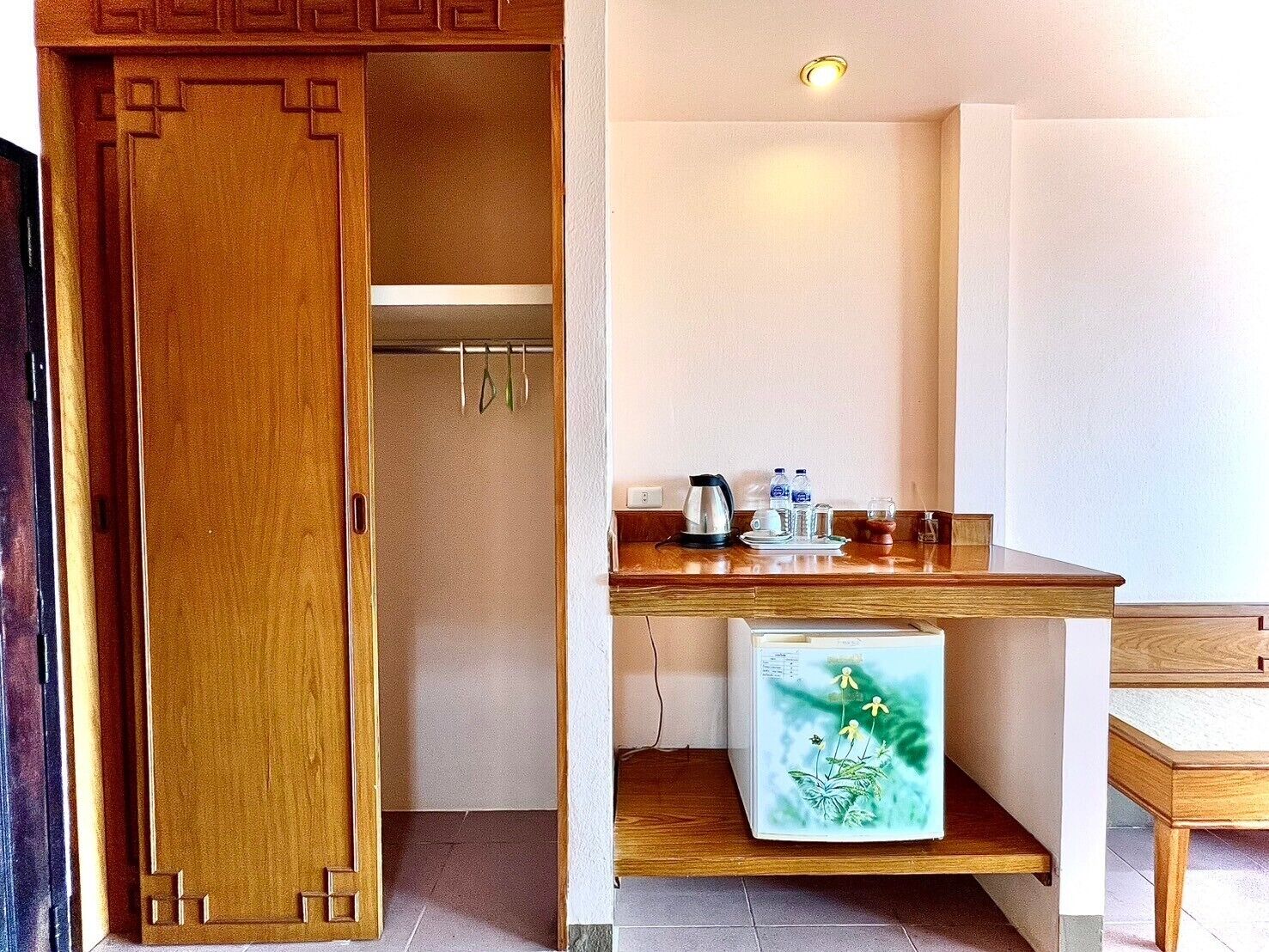 A compact room with a wooden door, a small kitchenette with a refrigerator, a coffee maker, and a water dispenser.