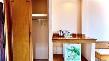 A compact room with a wooden door, a small kitchenette with a refrigerator, a coffee maker, and a water dispenser.