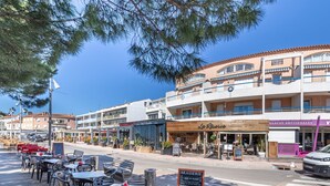 A coastal town with outdoor seating at a café, a restaurant, and a building with balconies.