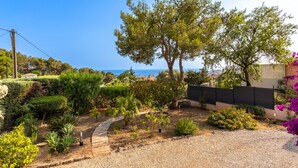 A garden with a gravel path, various plants, and a view of the sea.