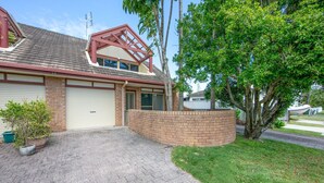 A two-story house with a garage, brick exterior, and a driveway leading to a gated entrance.