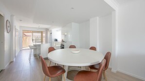 A modern kitchen with white cabinets, a central island, and a dining area with a round table and brown chairs.