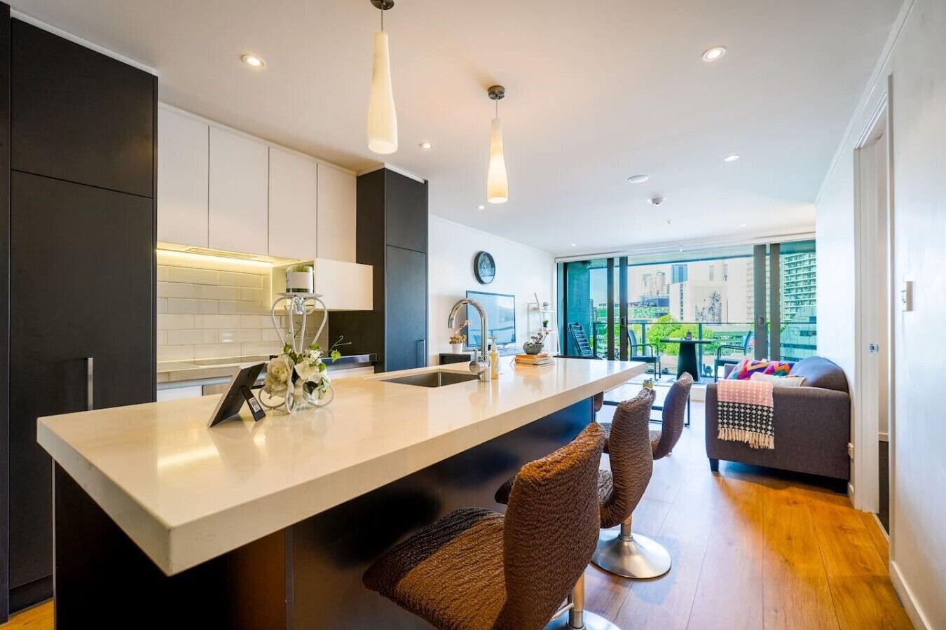 A modern kitchen with a central island, dark cabinetry, and a view to a balcony with outdoor seating.