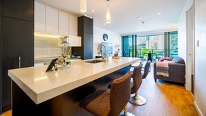 Une cuisine moderne dotée d’un îlot central, de meubles de rangement aux couleurs sombres et donnant sur un balcon aménagé avec un espace salon extérieur.