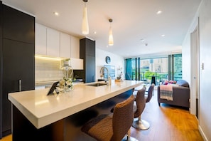 A modern kitchen with a central island, dark cabinetry, and a view to a balcony with outdoor seating.