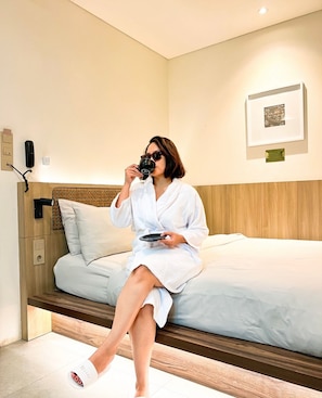 A person sitting on a bed in a hotel room, holding a plate and a cup. - Ustay Batik Style Hotel (Jakarta)