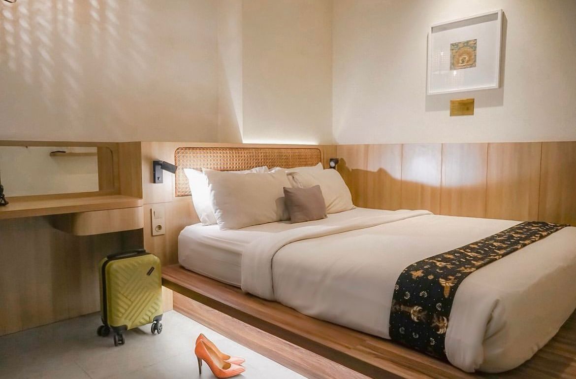 Een hotelkamer met een bed, een nachtkastje, een koffer en een paar hoge hakken.
