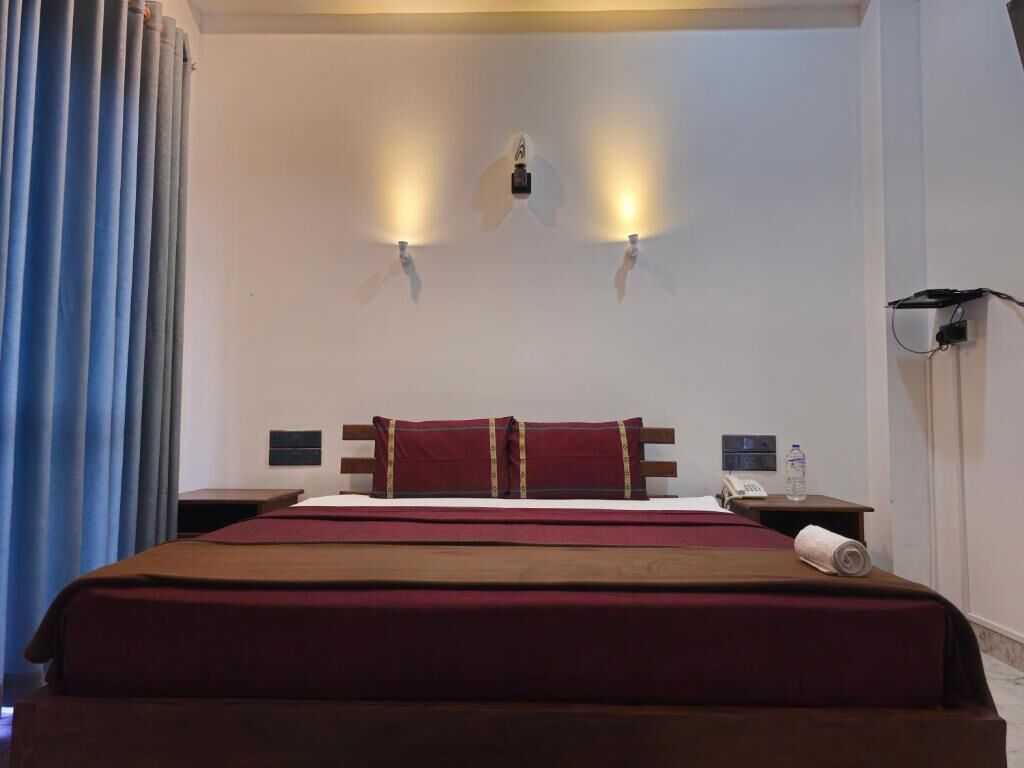 A hotel room with a large bed, two bedside tables, a nightstand, a lamp, and a curtain.