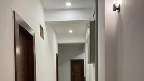 Un lungo e stretto corridoio con pavimento lucido, porte in legno e un punto luce a parete.