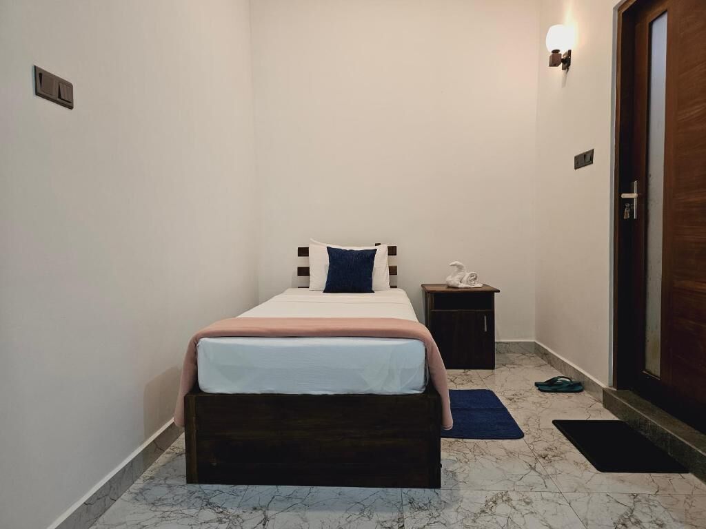 A small, neatly arranged bedroom with a single bed, a nightstand, a door, and a marble floor.