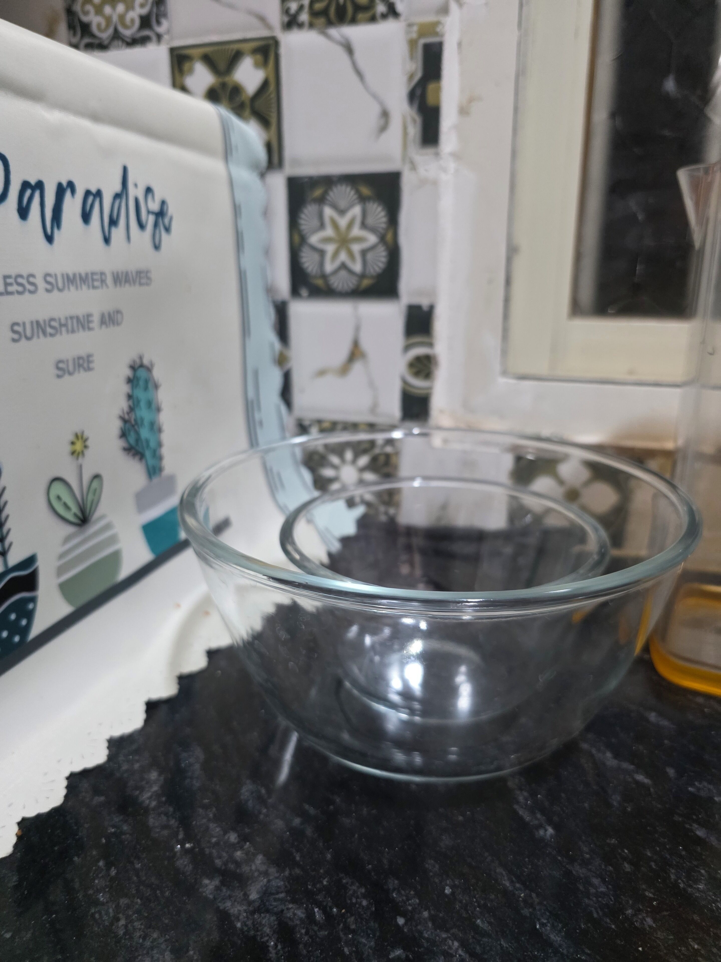 A clear glass bowl on a dark countertop, with a decorative box in the background featuring a cactus and text.