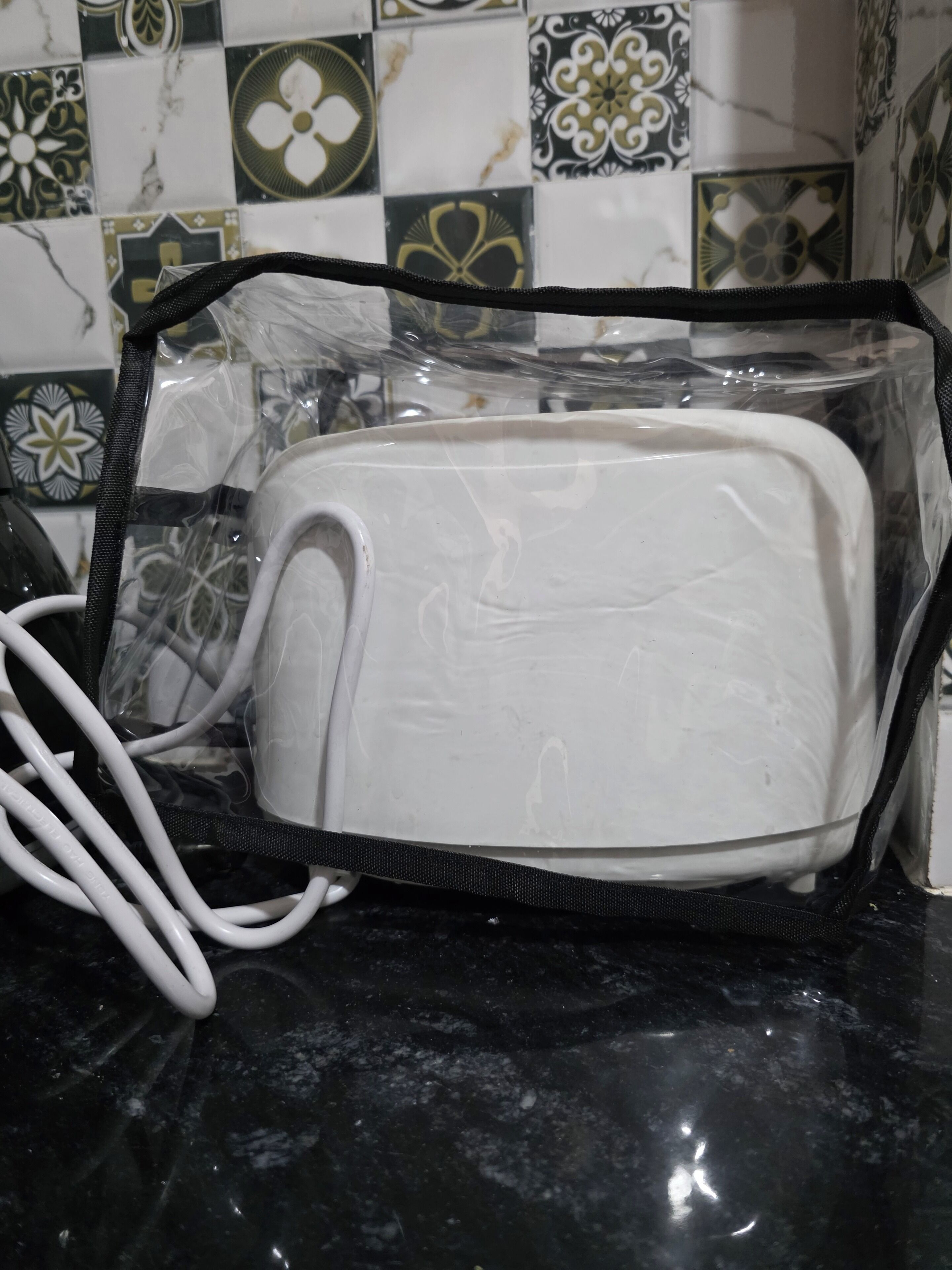 A white toaster in a clear plastic bag with a black zipper, placed on a black countertop.
