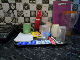 Una encimera de cocina con diversos objetos, incluyendo una taza verde, un cuchillo con mango rojo, un paquete de bocadillos y varios recipientes cilíndricos.