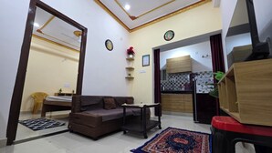 A living room with a sofa, a dining table, and a kitchen area with cabinets and a refrigerator. - Narayans Residency (Gaya)