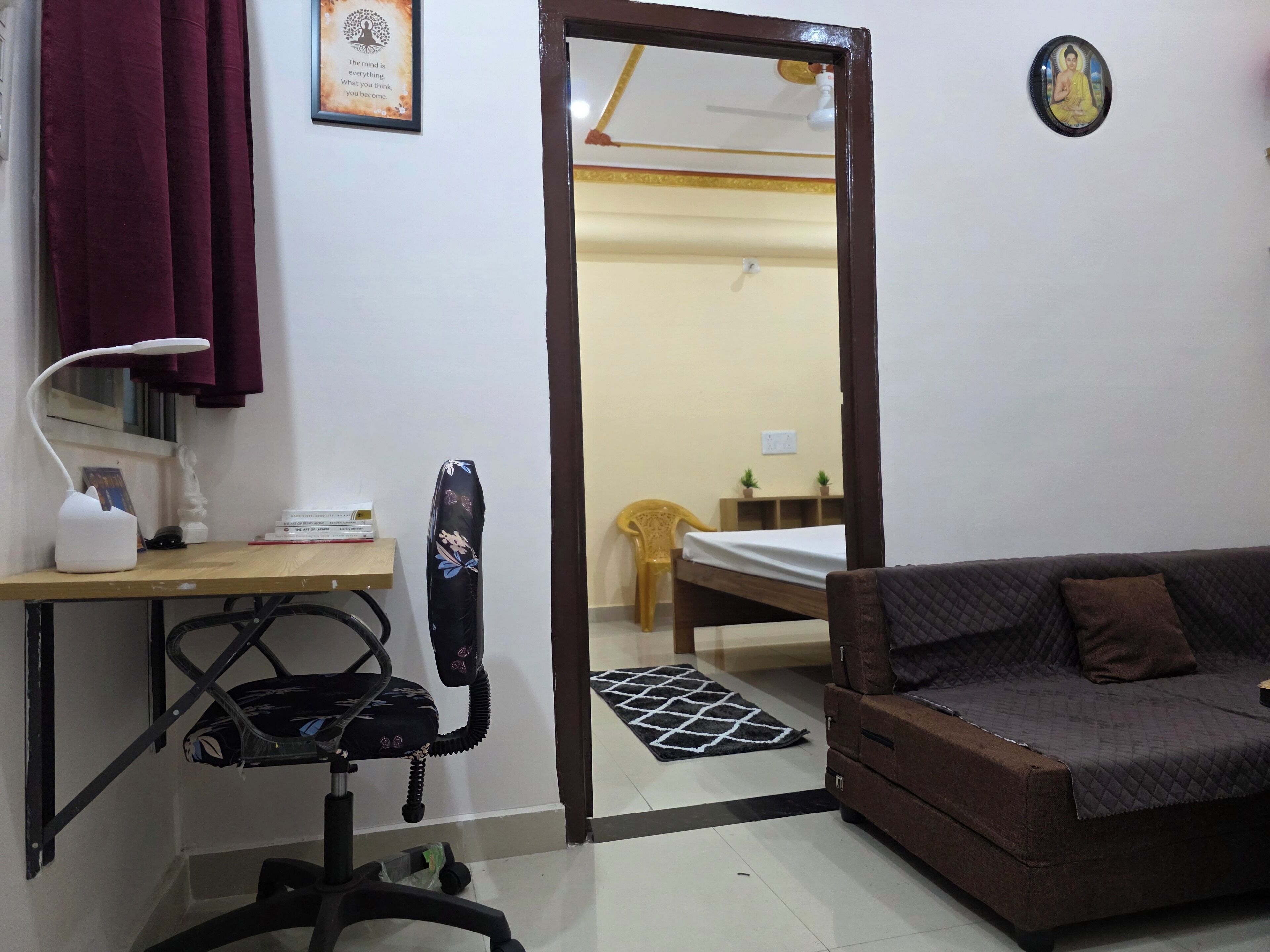 A compact room with a bed, a desk with a lamp, a chair, a sofa, and a mirror.