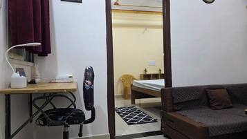 A compact room with a bed, a desk with a lamp, a chair, a sofa, and a mirror.