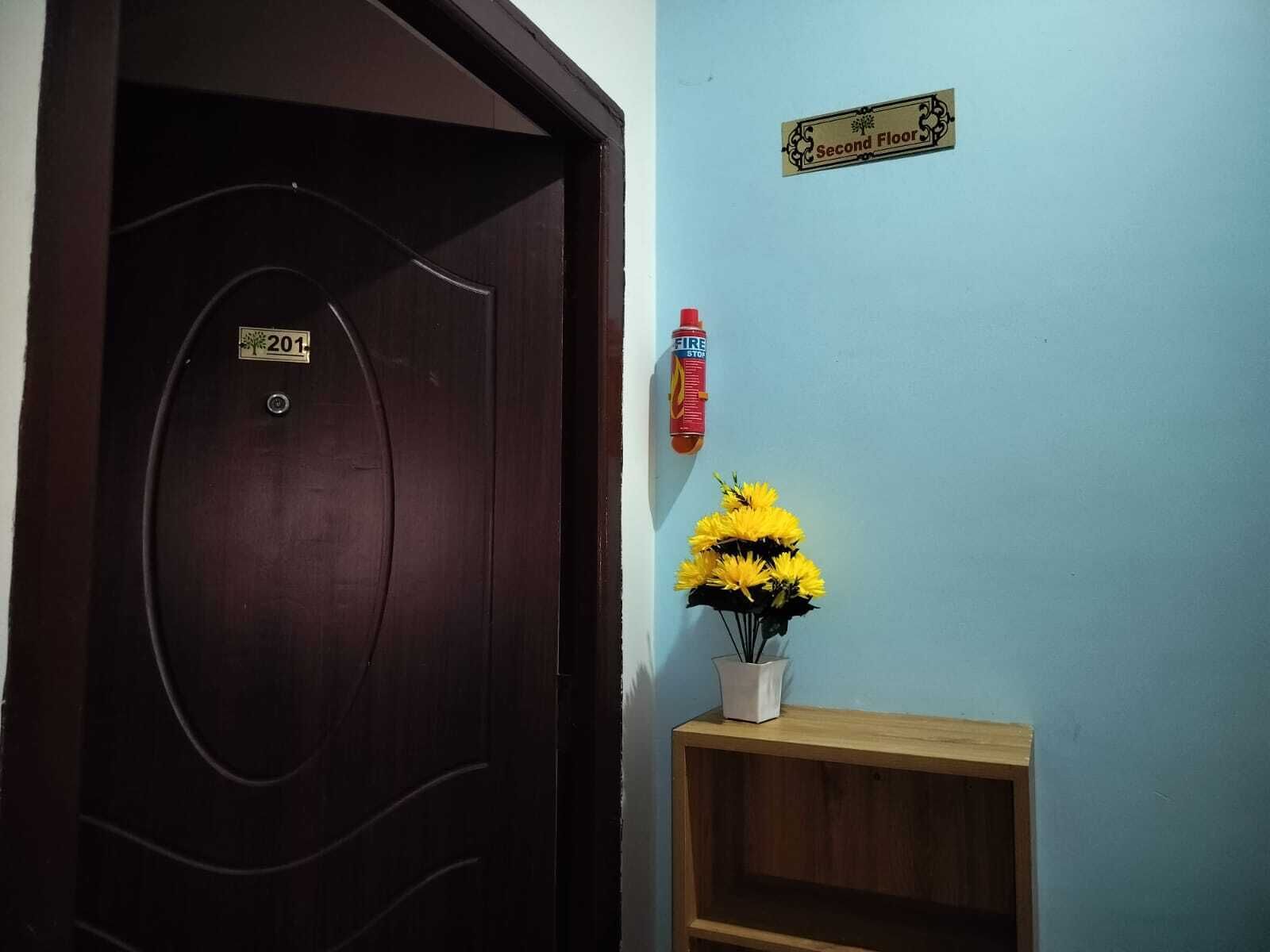 A door with a number plate, a fire extinguisher, and a flower vase on a shelf.