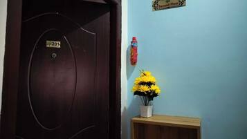 Una puerta con una placa de número, un extintor y un florero sobre una estantería.
