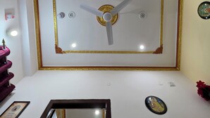 A room with a large wall clock, a ceiling fan, and a framed picture on the wall. - Narayans Residency (Gaya)
