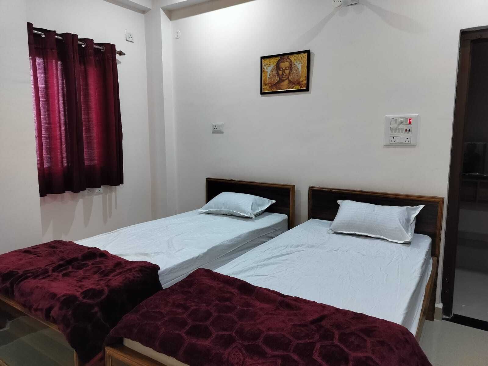 A room with two single beds, a red curtain, a wall-mounted power outlet, and a framed picture.