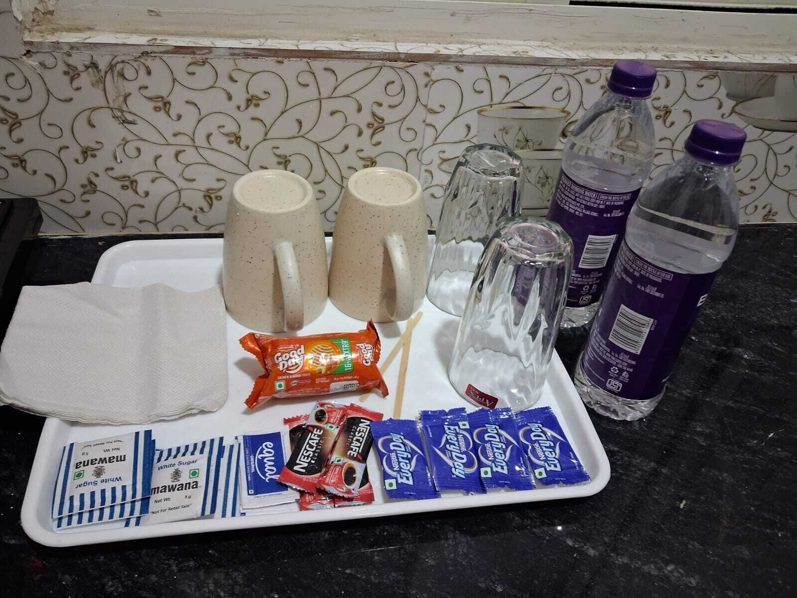 A tray with two mugs, a glass, a water bottle, and several snack packets.