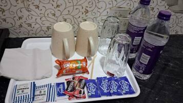 A tray with two mugs, a glass, a water bottle, and several snack packets.