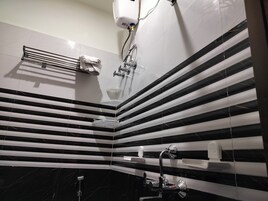 Un baño moderno con baldosas a rayas negras y blancas, un perchero, un cabezal de ducha y un secador de manos.