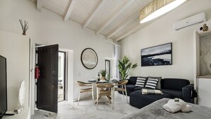 Un salon moderne avec un canapé foncé, une table à manger avec des chaises, un téléviseur et une grande fenêtre.