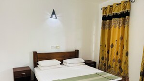 Un lit bien fait, avec du linge de lit blanc et une couverture à rayures vertes, une tête de lit en bois, une table de chevet et un luminaire fixé au mur.