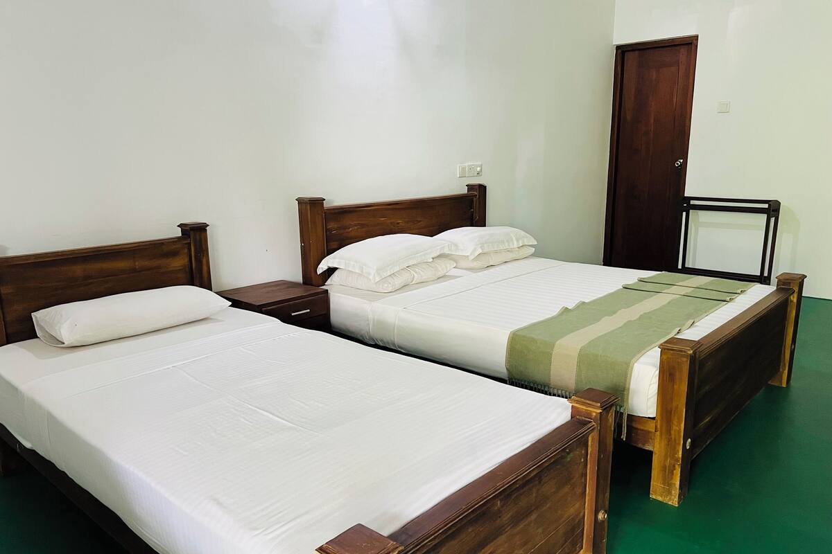 Ein Zimmer mit zwei Einzelbetten, Holz-Kopfteilen, einem grünen Boden und einem Holzschrank.
