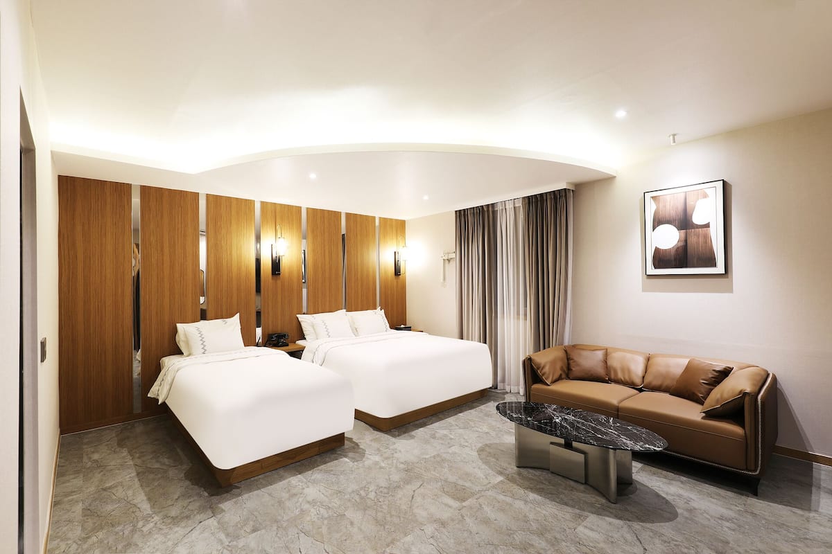 A hotel room with two beds, a sofa, a marble coffee table, and a large window with curtains.