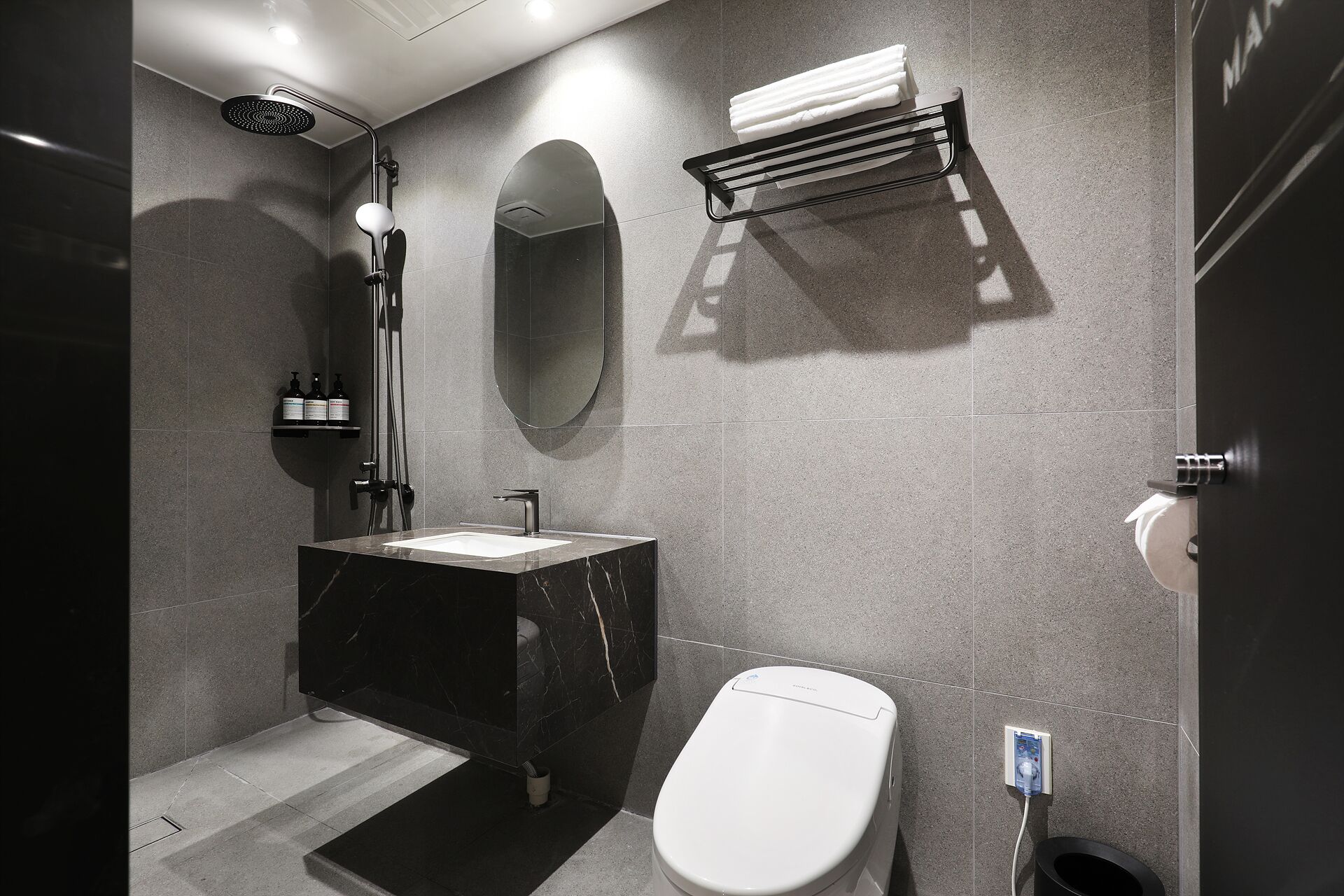 A modern bathroom with a marble sink, a toilet, a shower, and a towel rack.