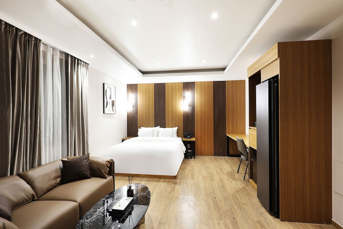 A modern hotel room with a bed, a sofa, a desk, and a television.
