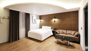 A modern hotel room with a large bed, a sofa, a coffee table, and a wooden panel wall. - marihotel (Seosan)