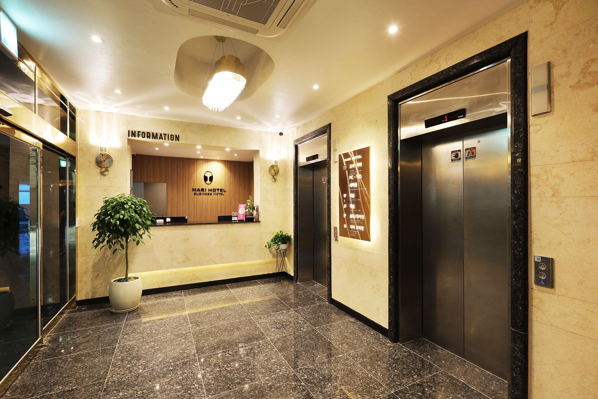 A hotel reception area with a reception desk, a plant, and two elevators.