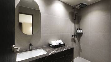 A modern bathroom with a marble sink, a large mirror, a shower, and toiletries on a shelf.