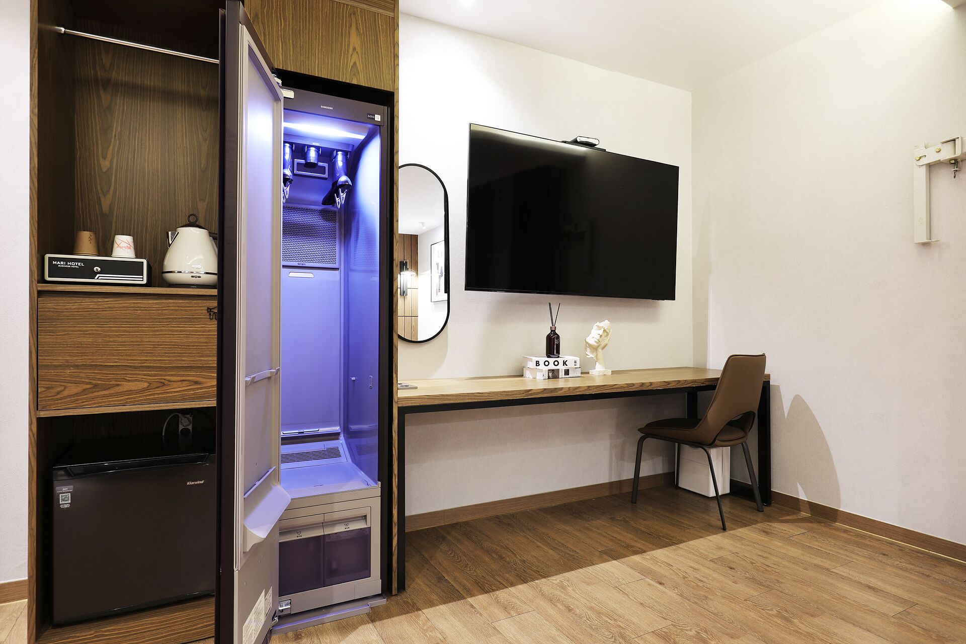 A hotel room with a minibar, a flat-screen TV, a wooden desk, and a chair.