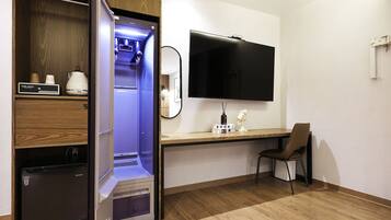 A hotel room with a minibar, a flat-screen TV, a wooden desk, and a chair.