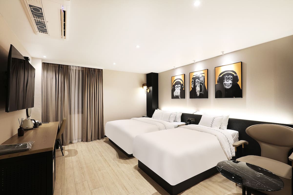 A hotel room with two beds, a desk, a chair, and artwork on the wall.