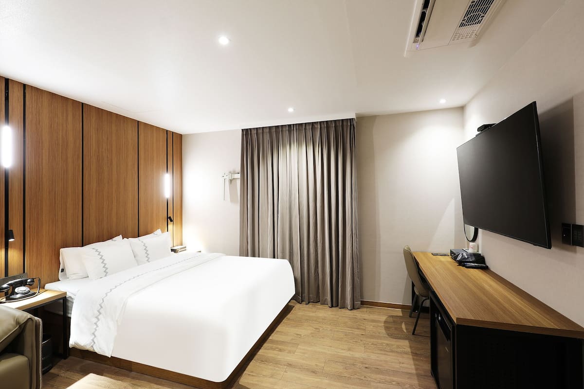 A hotel room with a bed, a desk, a television, and a window with curtains.