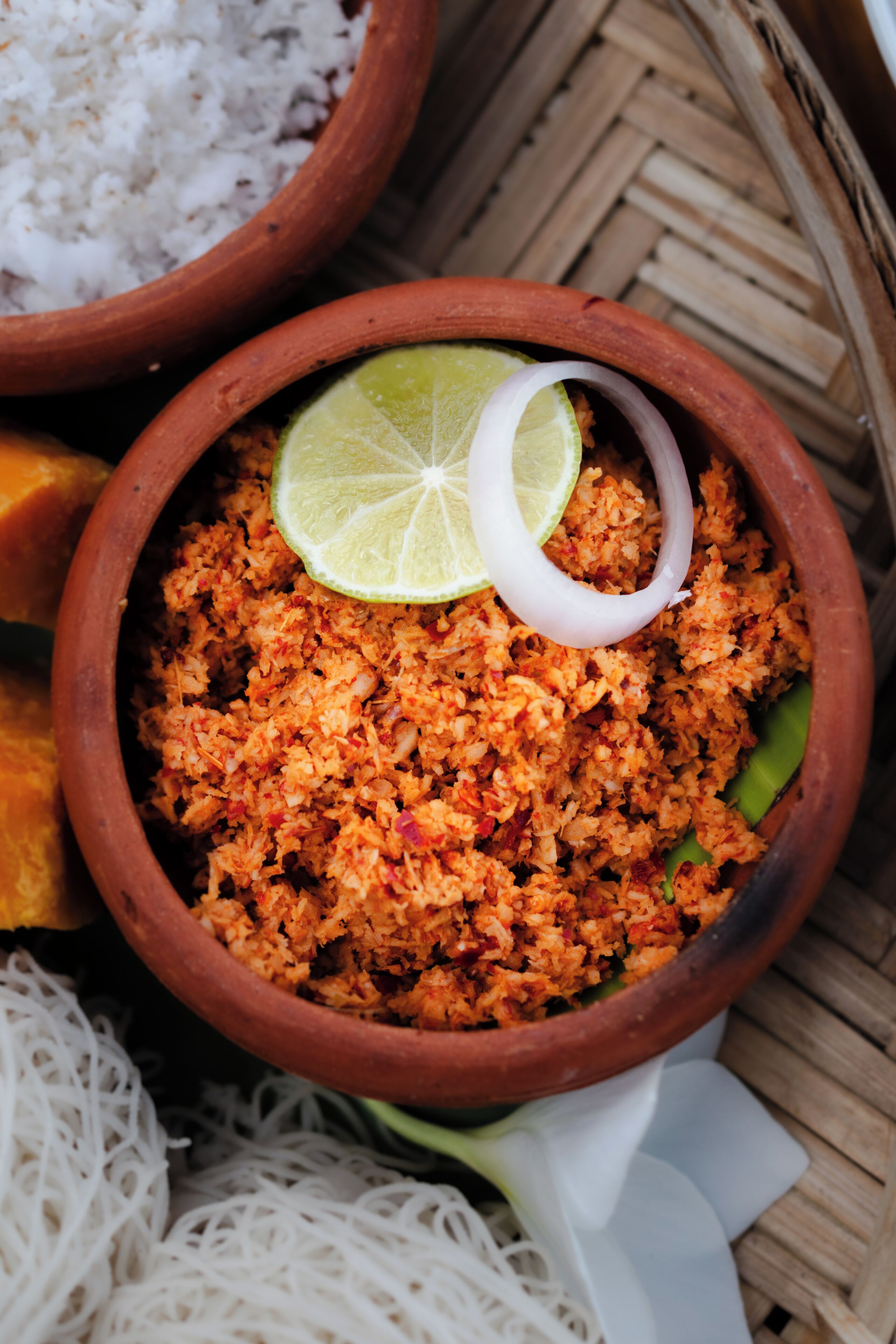 A bowl of seasoned rice garnished with a lime slice and onion, accompanied by white noodles and a bowl of white rice.