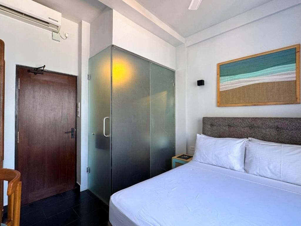 A hotel room with a bed, a wardrobe, a nightstand, and a painting on the wall.