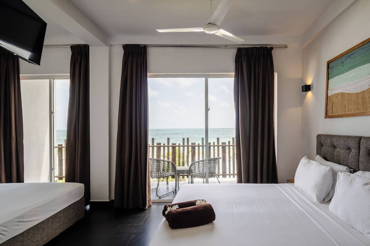 Een hotelkamer met een groot bed, een plafondventilator, een televisie en een balkon met uitzicht op zee.