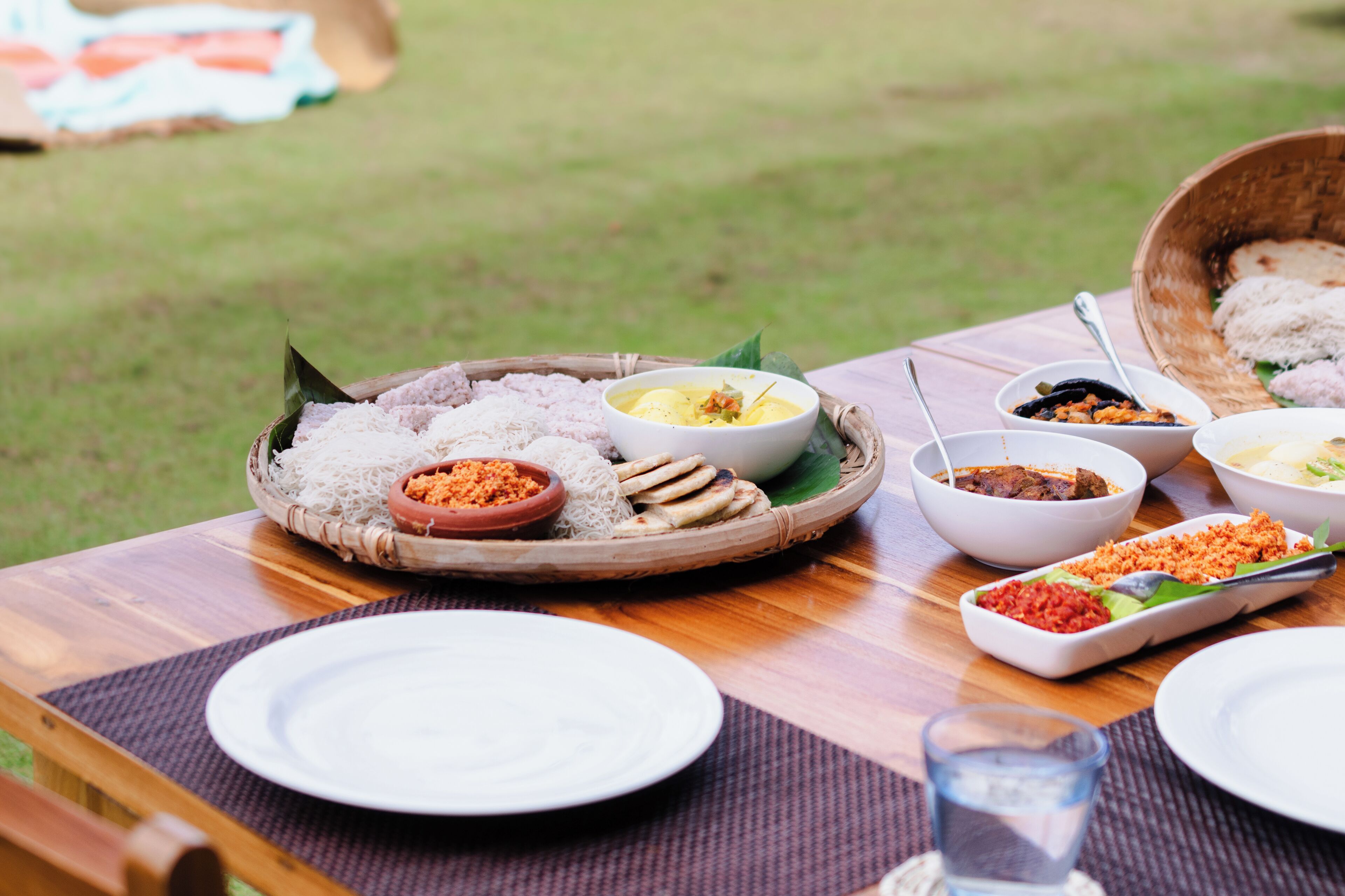 A table set outdoors with various dishes, including rice, soup, and side dishes, on a wooden table with a placemat.