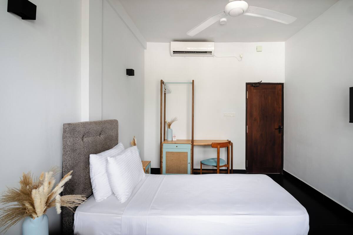 Een slaapkamer met een bed, een bureau, een stoel, een kledingkast en een airconditioning.